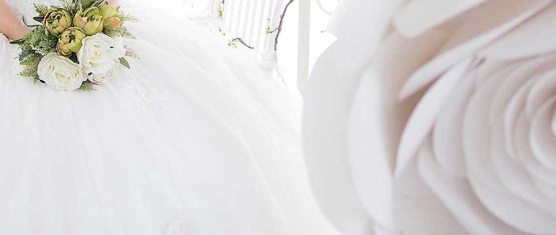 Bride in white dress holding bouquet of flowers, white rose in foreground.
